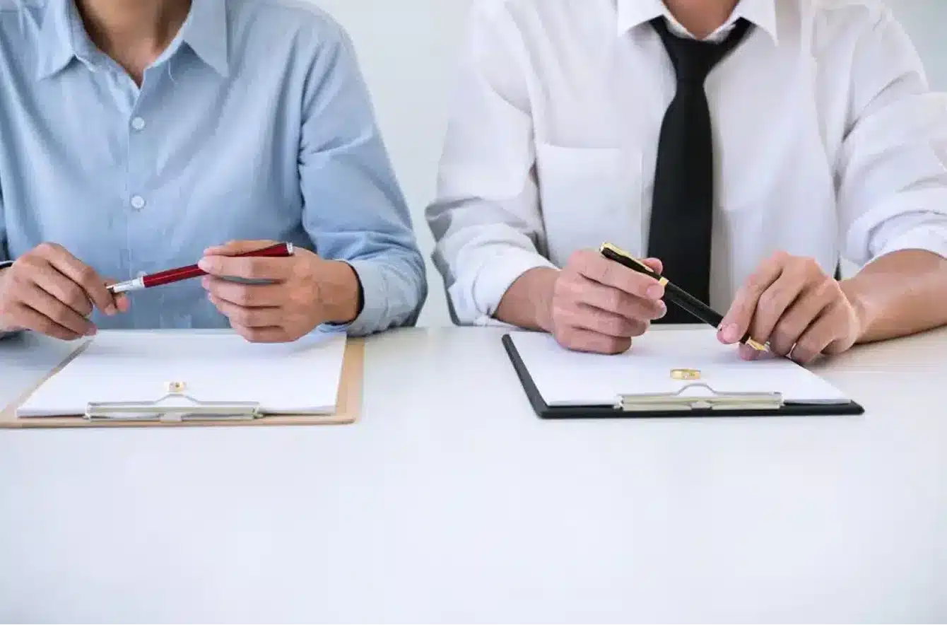 Two people seated at a table holding pens with clipboards in front of them