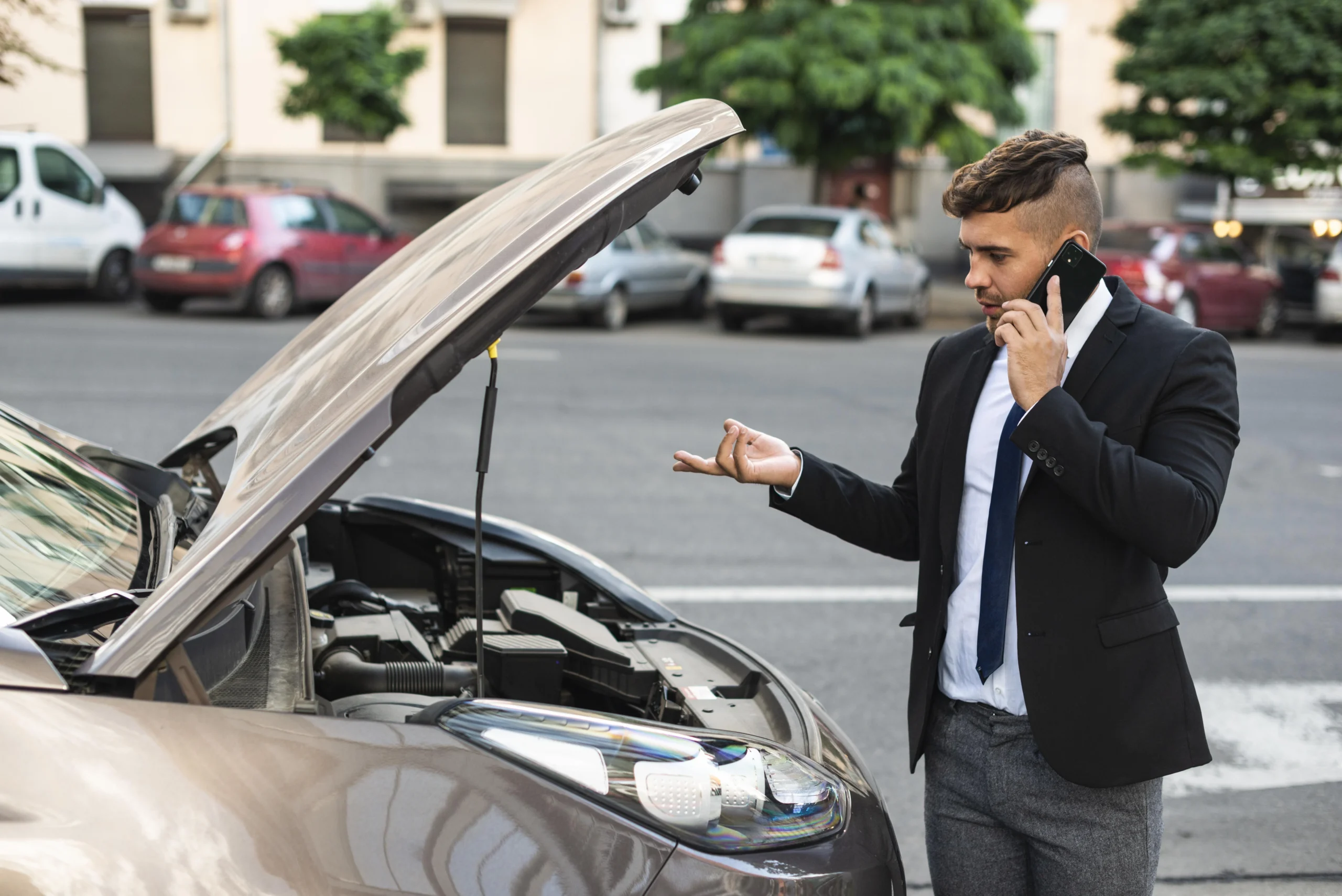 Man standing beside a car with the hood open after a breakdown or crash, speaking on the phone to a car accident lawyer.