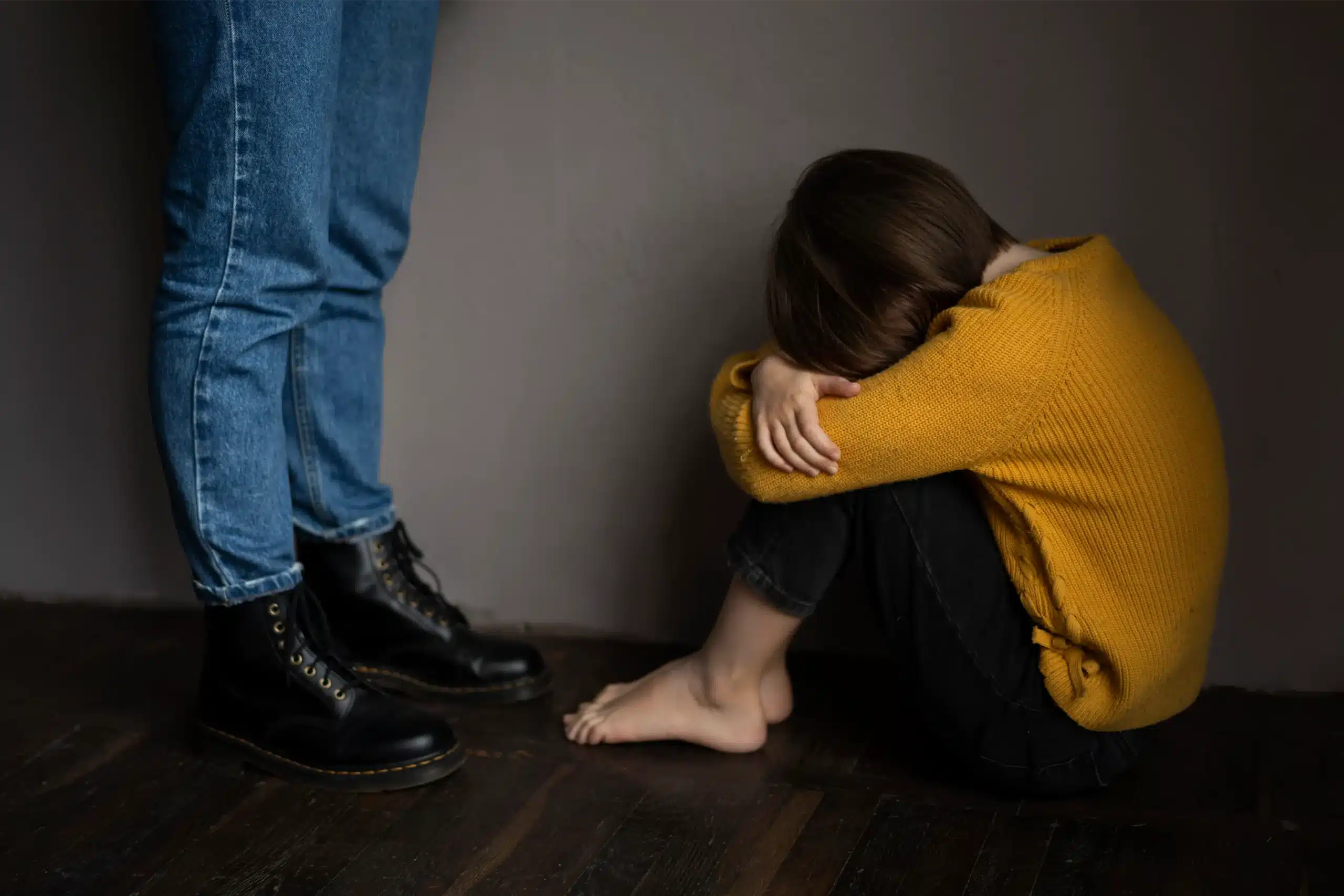 Child sitting on floor, hugging knees.